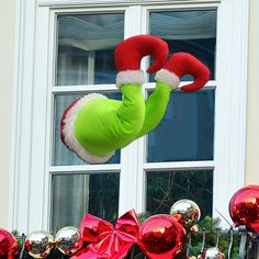 an inflatable person wearing a santa hat and green bodysuit is suspended from a window