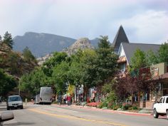 cars are driving down the street in front of houses with mountains in the back ground