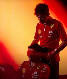 a man getting his hair cut by another man in front of an orange background with red lights