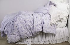 an unmade bed with purple and white comforter on it's headboard