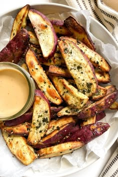 baked potato wedges with dipping sauce in a white bowl on a striped cloth tablecloth