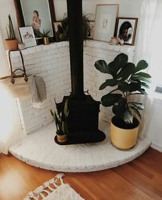 a living room with a white brick fireplace and potted plants on the corner table