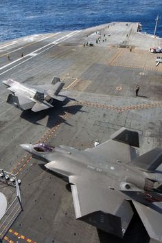 two fighter jets are parked on the flight deck of an aircraft carrier in the ocean