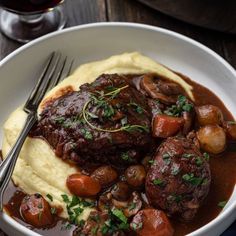 a bowl filled with meat and potatoes covered in gravy next to a glass of wine