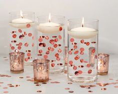 candles are lined up in glass vases with confetti on them