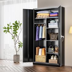 an open black cabinet with clothes and baskets in it next to a potted plant