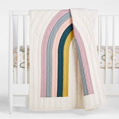 a white crib with a rainbow quilt on it