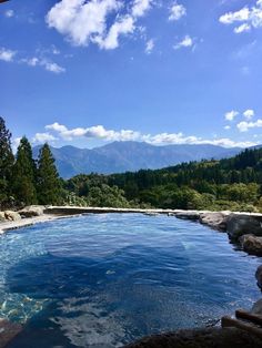 an outdoor swimming pool surrounded by rocks and trees with mountains in the background on a sunny day