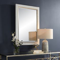 a table with a lamp, mirror and vase on it in front of a blue wall