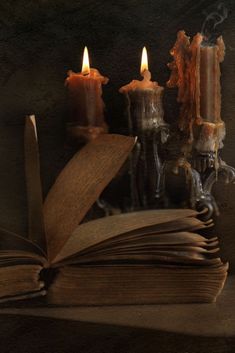 an open book sitting next to two lit candles