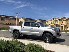 a silver truck parked on the side of a road in front of some houses and bushes