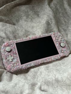 a pink nintendo wii game console sitting on top of a white bed sheet covered in beads