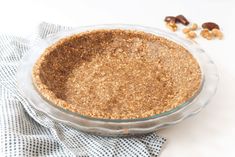 a pie crust in a glass dish on top of a blue and white towel next to nuts