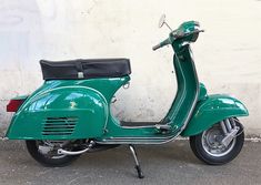 a green scooter parked next to a white wall