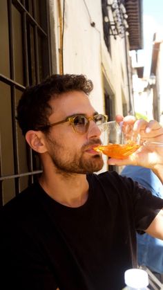 a man drinking water out of a plastic bottle in front of a wall with windows