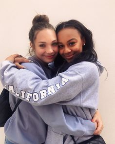 two young women hugging each other in front of a white wall with the words california on it