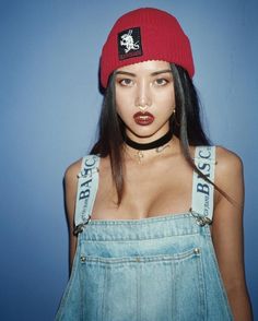 a woman wearing a red hat and denim overalls is posing for a photo in front of a blue background