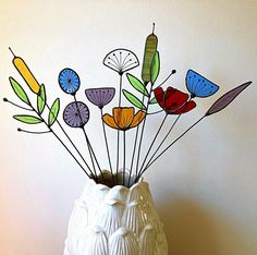 a white vase filled with lots of colorful flowers on top of a wooden table next to a wall