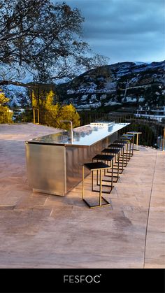 an outdoor kitchen with bar stools on the side and mountains in the back ground