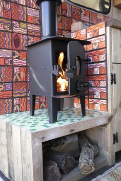 a wood burning stove sitting on top of a wooden table next to a wall covered in colorful tiles