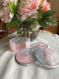 pink and white flowers in a glass vase on a table with two coasters next to it