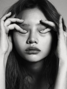 a woman holding her hands up to her eyes with both hands on her head and looking at the camera