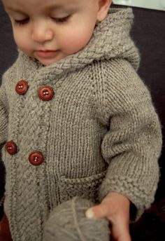 a baby wearing a sweater and holding a ball of yarn