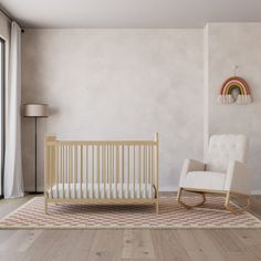 a baby's room with a rocking chair, crib and rainbow wall hanging