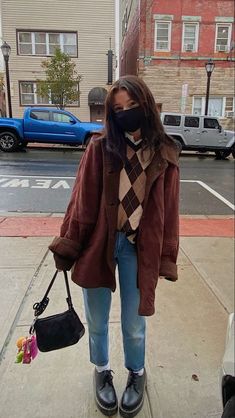 a woman standing on the sidewalk with her face covered by a mask and holding a handbag