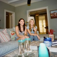 two young women sitting on a couch in a living room with blue and white decor