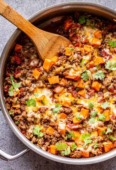 a large pot filled with meat and vegetables next to a wooden spoon on top of a table