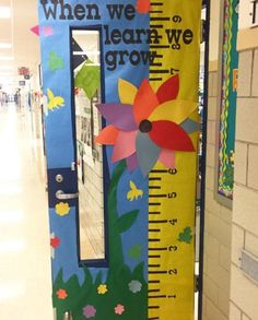 a door decorated like a growth chart with flowers and leaves on it, in the hallway of a school