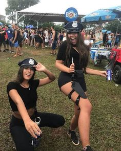 two women dressed in police uniforms sitting on the ground at an outdoor music festival with people standing around