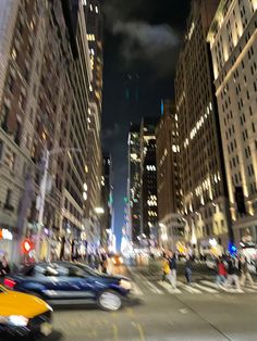 a city street filled with lots of tall buildings at night, traffic lights and people walking on the sidewalk