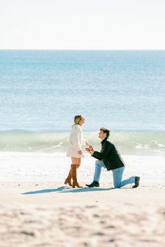 a man kneeling down next to a woman on the beach