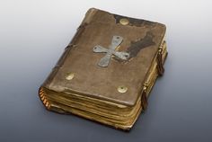 an old book with a cross on the cover is sitting on a reflective surface in front of a white background