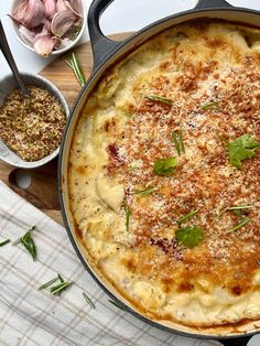 a baked dish with cheese and herbs on a table next to garlic, seasoning and spices