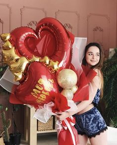 a woman holding two heart shaped balloons in her hands and posing for the camera,