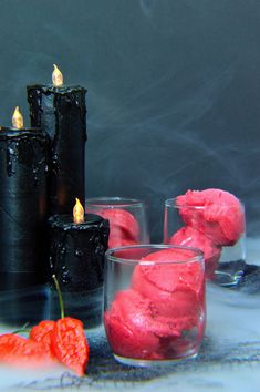 three candles and two glasses filled with pink frosting next to some red strawberries