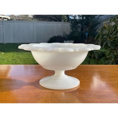 a white bowl sitting on top of a wooden table in front of a fenced yard