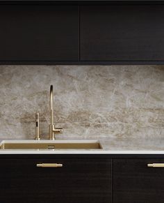 a kitchen with marble counter tops and gold faucets on the sink, along with dark wood cabinets