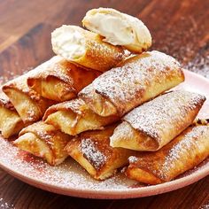 some crepes are on a pink plate with powdered sugar and ice cream