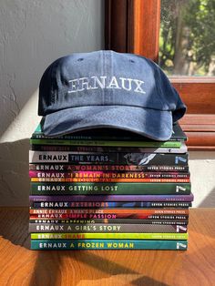 a stack of books sitting on top of a wooden table next to a baseball cap