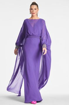 a woman wearing a purple dress with sheer sleeves and an embellishment on the waist