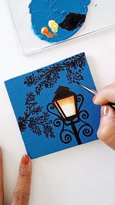 someone is painting on a piece of blue paper with a lamp post in the background