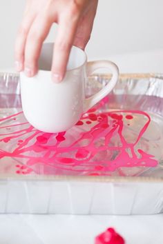 someone is pouring liquid into a cup on top of a tray with pink and white paint