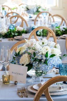 the table is set with blue and white flowers in vases, silverware, and place cards