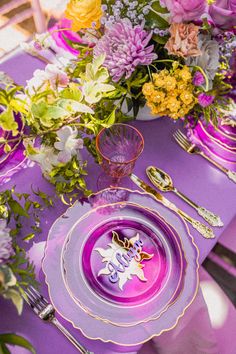 the table is set with purple and yellow plates, silverware, and floral centerpieces