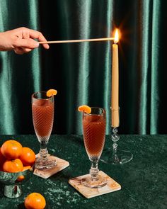 two glasses filled with liquid and oranges sitting on a table next to a candle