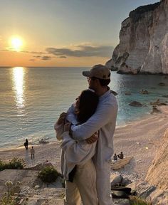 a man and woman hug on the beach as the sun sets